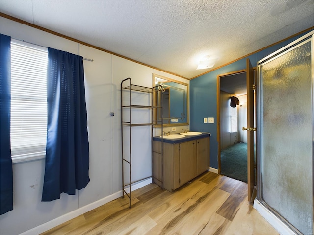 bathroom featuring walk in shower, wood-type flooring, a textured ceiling, vanity, and ornamental molding