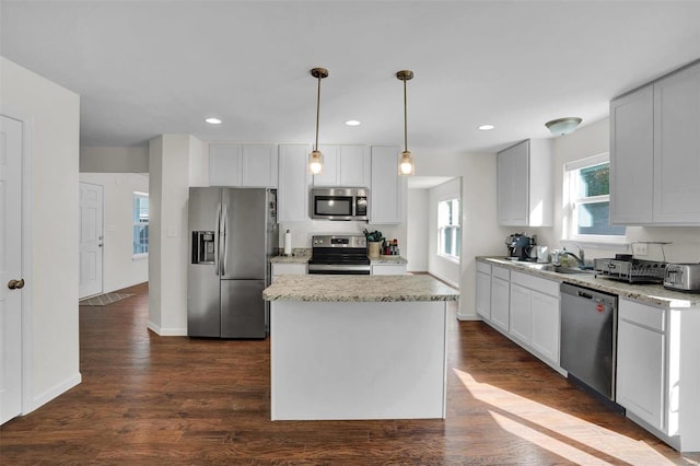 kitchen featuring dark wood-type flooring, appliances with stainless steel finishes, decorative light fixtures, a kitchen island, and white cabinetry