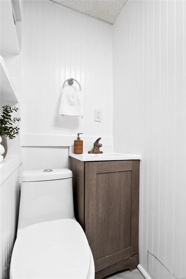 bathroom with vanity, a drop ceiling, toilet, and wooden walls