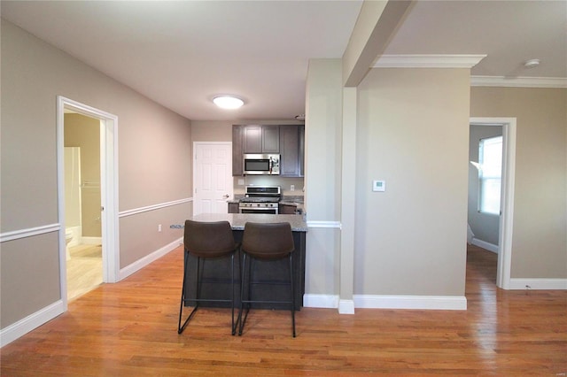 kitchen featuring crown molding, a breakfast bar, stainless steel appliances, and light wood-type flooring