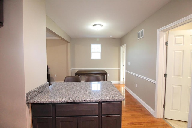 kitchen with light stone countertops, dark brown cabinetry, and light hardwood / wood-style flooring