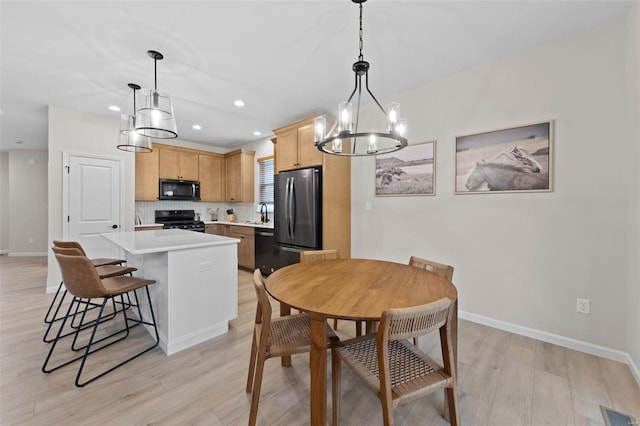 kitchen with light brown cabinetry, decorative light fixtures, a center island, light hardwood / wood-style flooring, and black appliances