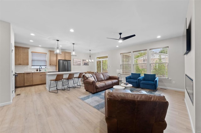 living room with ceiling fan with notable chandelier, plenty of natural light, sink, and light wood-type flooring