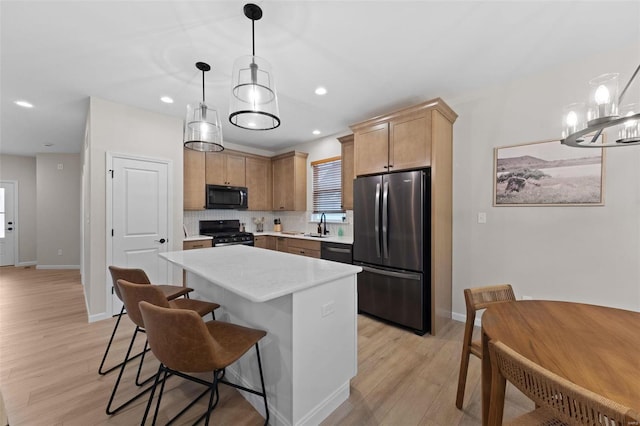 kitchen with pendant lighting, a center island, tasteful backsplash, light hardwood / wood-style floors, and black appliances