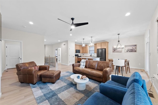 living room with ceiling fan with notable chandelier and light hardwood / wood-style flooring