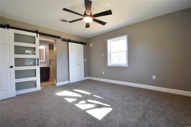 unfurnished bedroom featuring a barn door, ceiling fan, a closet, and carpet