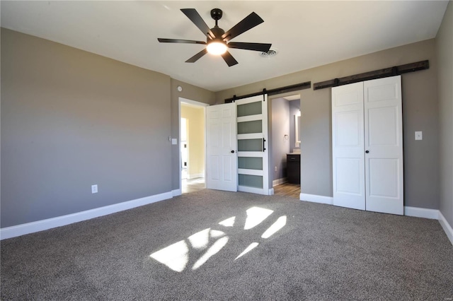 unfurnished bedroom with ensuite bath, ceiling fan, a barn door, carpet floors, and a closet