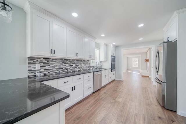 kitchen with appliances with stainless steel finishes, sink, light hardwood / wood-style flooring, white cabinets, and hanging light fixtures