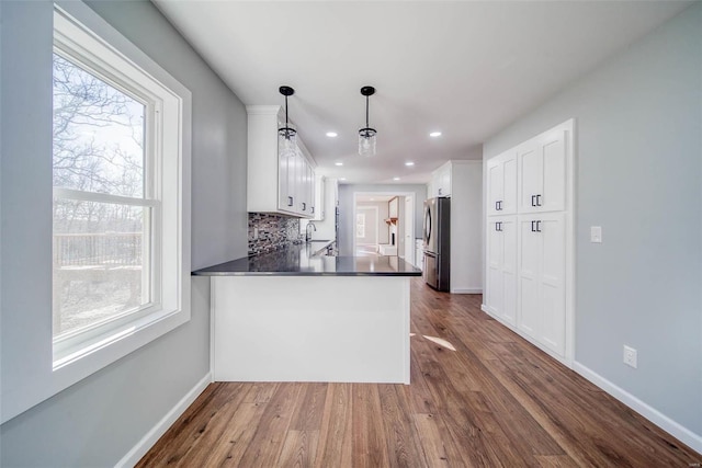 kitchen featuring white cabinets, kitchen peninsula, hanging light fixtures, and stainless steel refrigerator