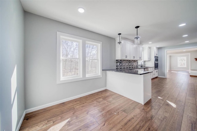 kitchen with kitchen peninsula, sink, hardwood / wood-style flooring, white cabinets, and hanging light fixtures