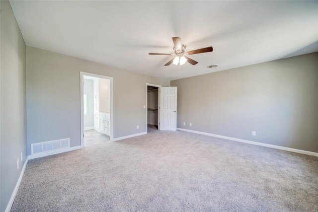 unfurnished bedroom featuring ceiling fan, a walk in closet, light carpet, and ensuite bath