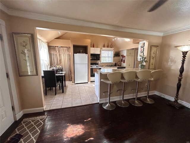 kitchen featuring white cabinetry, light hardwood / wood-style flooring, lofted ceiling, white appliances, and a breakfast bar