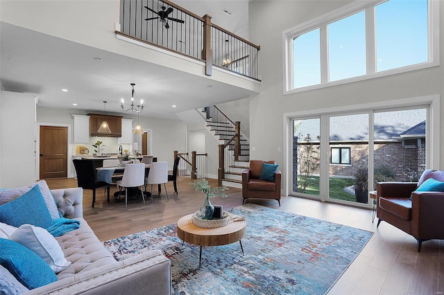 living room featuring ceiling fan with notable chandelier, light hardwood / wood-style floors, and a towering ceiling