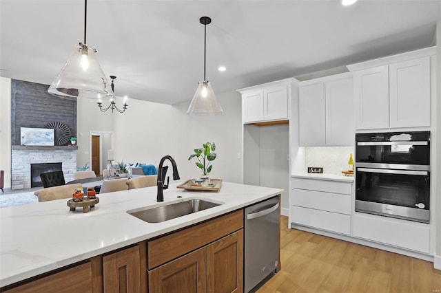 kitchen with sink, stainless steel appliances, decorative light fixtures, a fireplace, and white cabinets