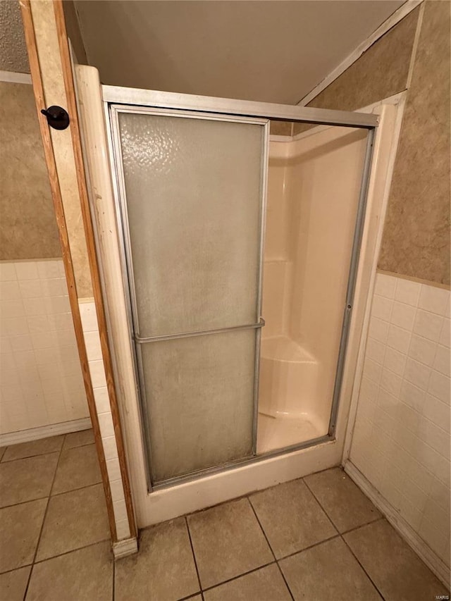 bathroom with tile patterned flooring, a shower with door, and tile walls