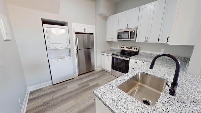 kitchen with white cabinetry, sink, stainless steel appliances, and stacked washer and clothes dryer