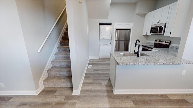 kitchen featuring appliances with stainless steel finishes, stacked washing maching and dryer, light stone counters, sink, and white cabinets