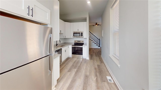 kitchen featuring light wood-type flooring, light stone counters, stainless steel appliances, sink, and white cabinets