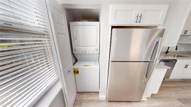 laundry room featuring light hardwood / wood-style flooring, a healthy amount of sunlight, sink, and stacked washer and clothes dryer