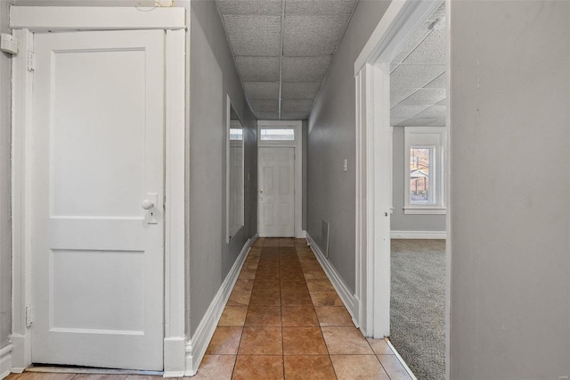 hall featuring a paneled ceiling and light tile patterned floors