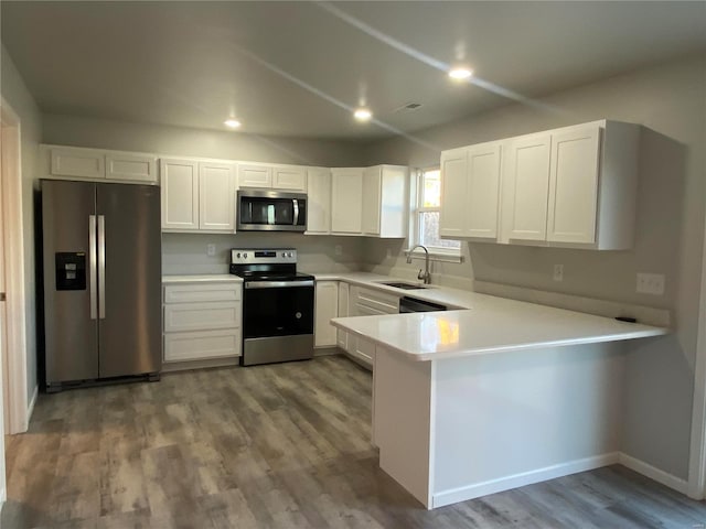 kitchen with kitchen peninsula, appliances with stainless steel finishes, sink, wood-type flooring, and white cabinets