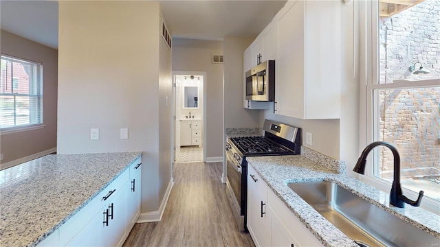 kitchen featuring white cabinetry, sink, light stone counters, and appliances with stainless steel finishes