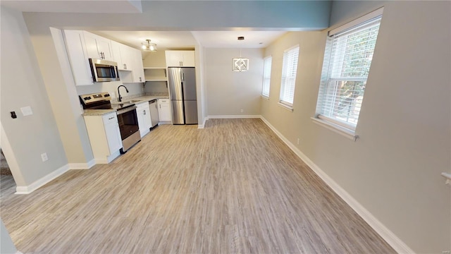 kitchen with light stone countertops, light wood-type flooring, appliances with stainless steel finishes, decorative light fixtures, and white cabinetry