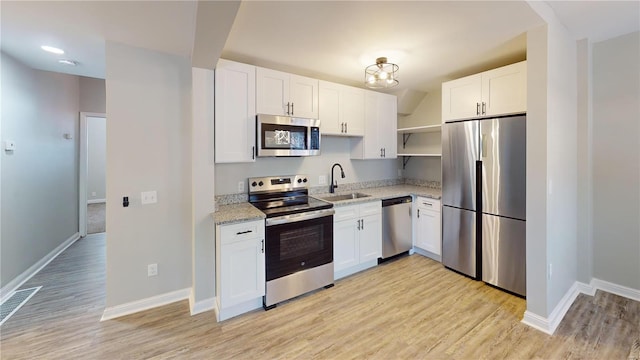 kitchen with appliances with stainless steel finishes, light hardwood / wood-style floors, white cabinetry, and sink