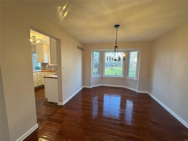 unfurnished dining area featuring a notable chandelier and dark hardwood / wood-style flooring