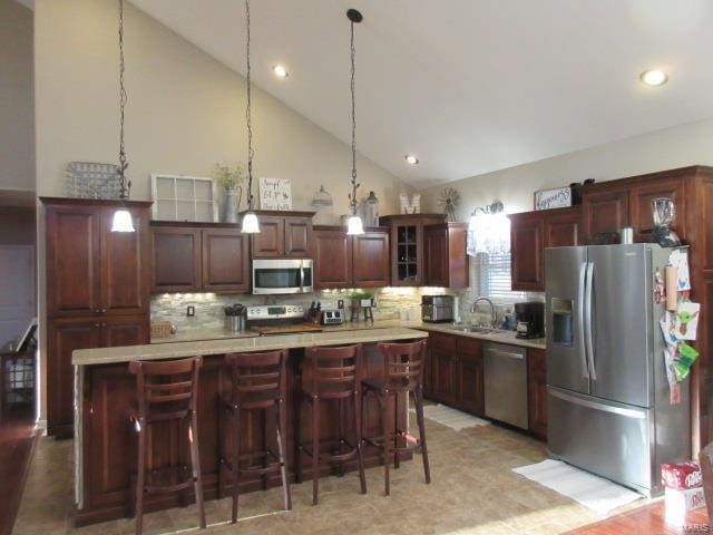 kitchen with high vaulted ceiling, hanging light fixtures, sink, a kitchen island, and stainless steel appliances