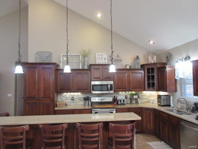 kitchen with a kitchen bar, appliances with stainless steel finishes, tasteful backsplash, sink, and high vaulted ceiling