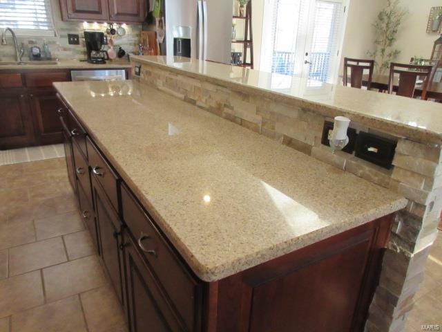 kitchen with backsplash, light stone counters, sink, and stainless steel refrigerator with ice dispenser