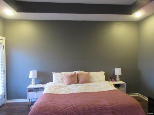 bedroom with dark hardwood / wood-style floors and a raised ceiling