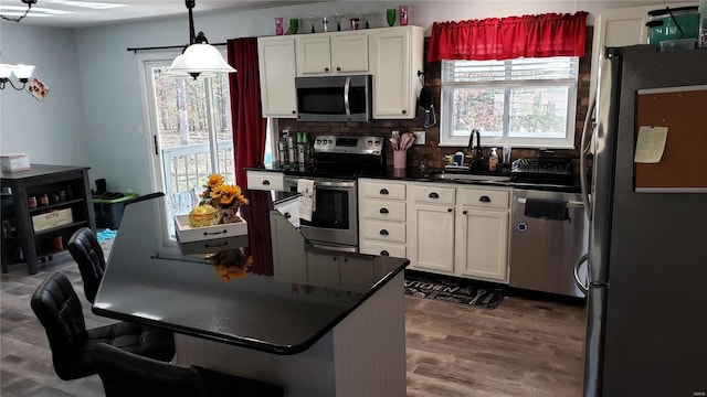 kitchen featuring sink, white cabinets, decorative light fixtures, and appliances with stainless steel finishes