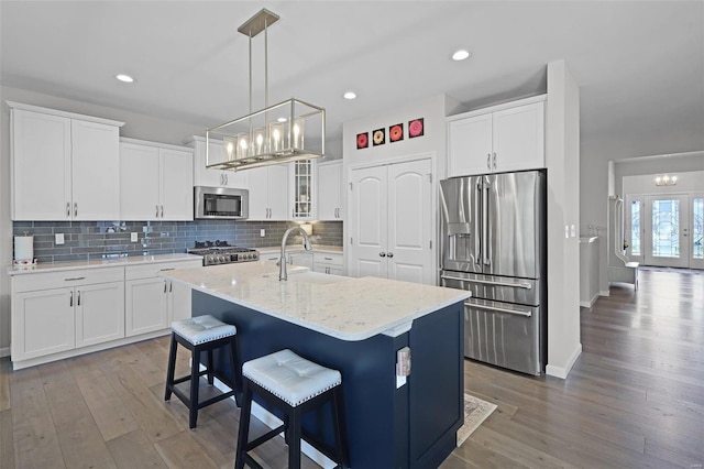 kitchen featuring hardwood / wood-style floors, a kitchen island with sink, sink, appliances with stainless steel finishes, and white cabinetry