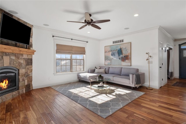 living room featuring a stone fireplace, ceiling fan, ornamental molding, wood-type flooring, and heating unit