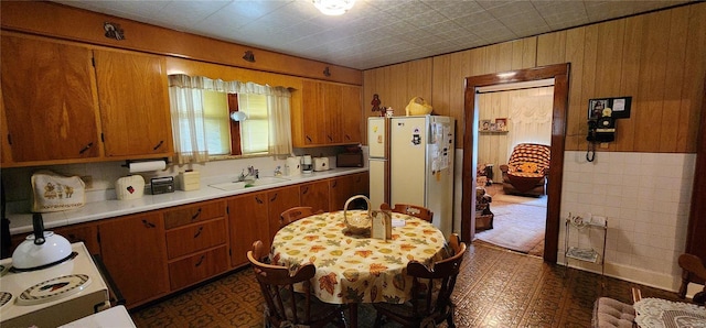 kitchen featuring white fridge, wooden walls, and sink