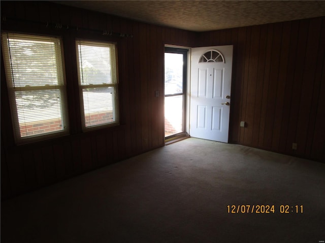 carpeted foyer entrance with a textured ceiling and wood walls