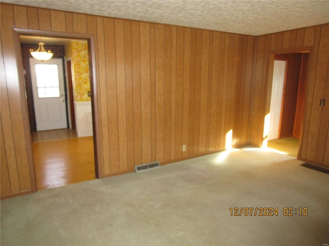 carpeted empty room featuring wooden walls and a textured ceiling