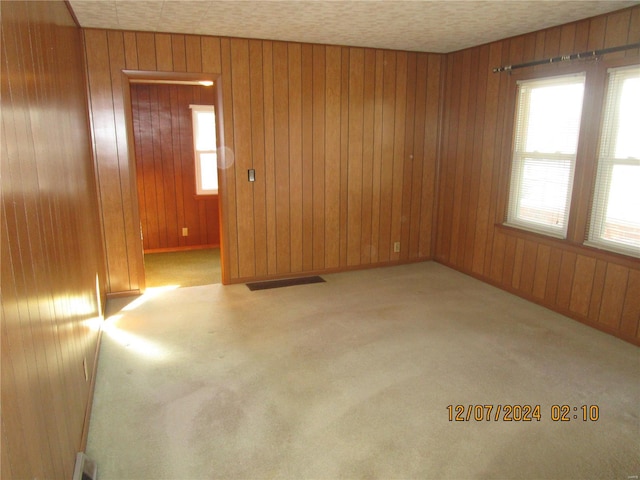 unfurnished room with light colored carpet, a textured ceiling, and wood walls