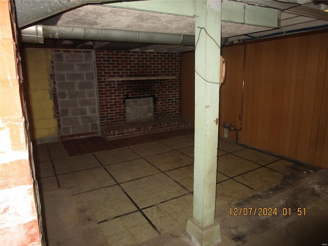 basement featuring a brick fireplace and wood walls