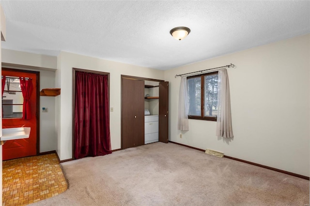 unfurnished bedroom featuring light carpet, a textured ceiling, and washer / clothes dryer