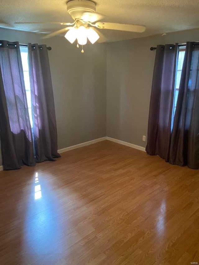 empty room with hardwood / wood-style flooring, ceiling fan, a healthy amount of sunlight, and a textured ceiling