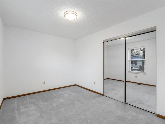 unfurnished bedroom featuring light colored carpet, a textured ceiling, and a closet