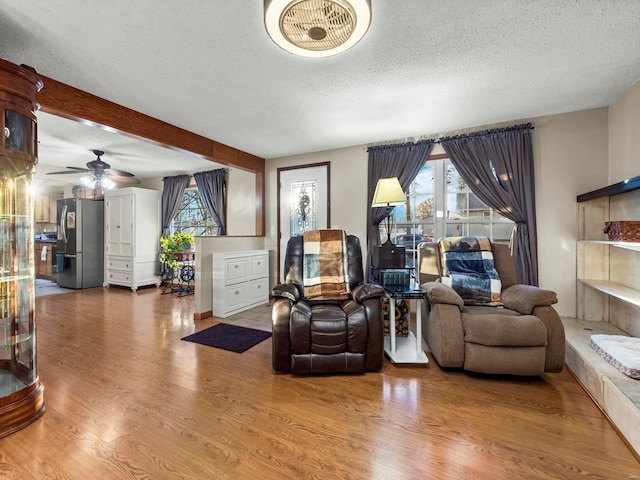 living room with beam ceiling, ceiling fan, a textured ceiling, and hardwood / wood-style flooring