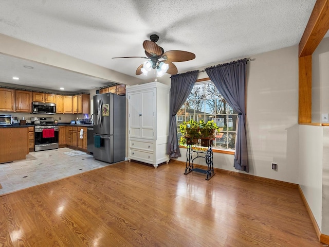 kitchen with a textured ceiling, light wood-type flooring, stainless steel appliances, and ceiling fan