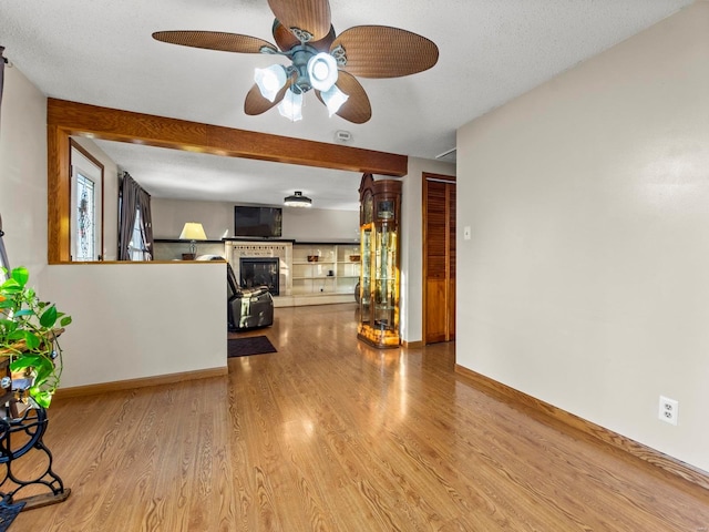 living room featuring ceiling fan, light hardwood / wood-style floors, a textured ceiling, and a brick fireplace