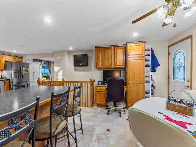 kitchen with a textured ceiling, ceiling fan, and stainless steel refrigerator with ice dispenser