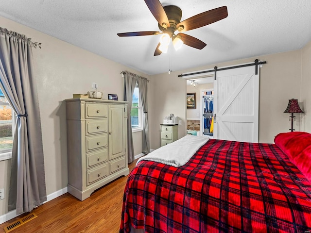 bedroom featuring a barn door, ceiling fan, multiple windows, and hardwood / wood-style flooring