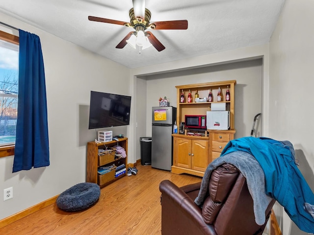 living room with a textured ceiling, light wood-type flooring, and ceiling fan